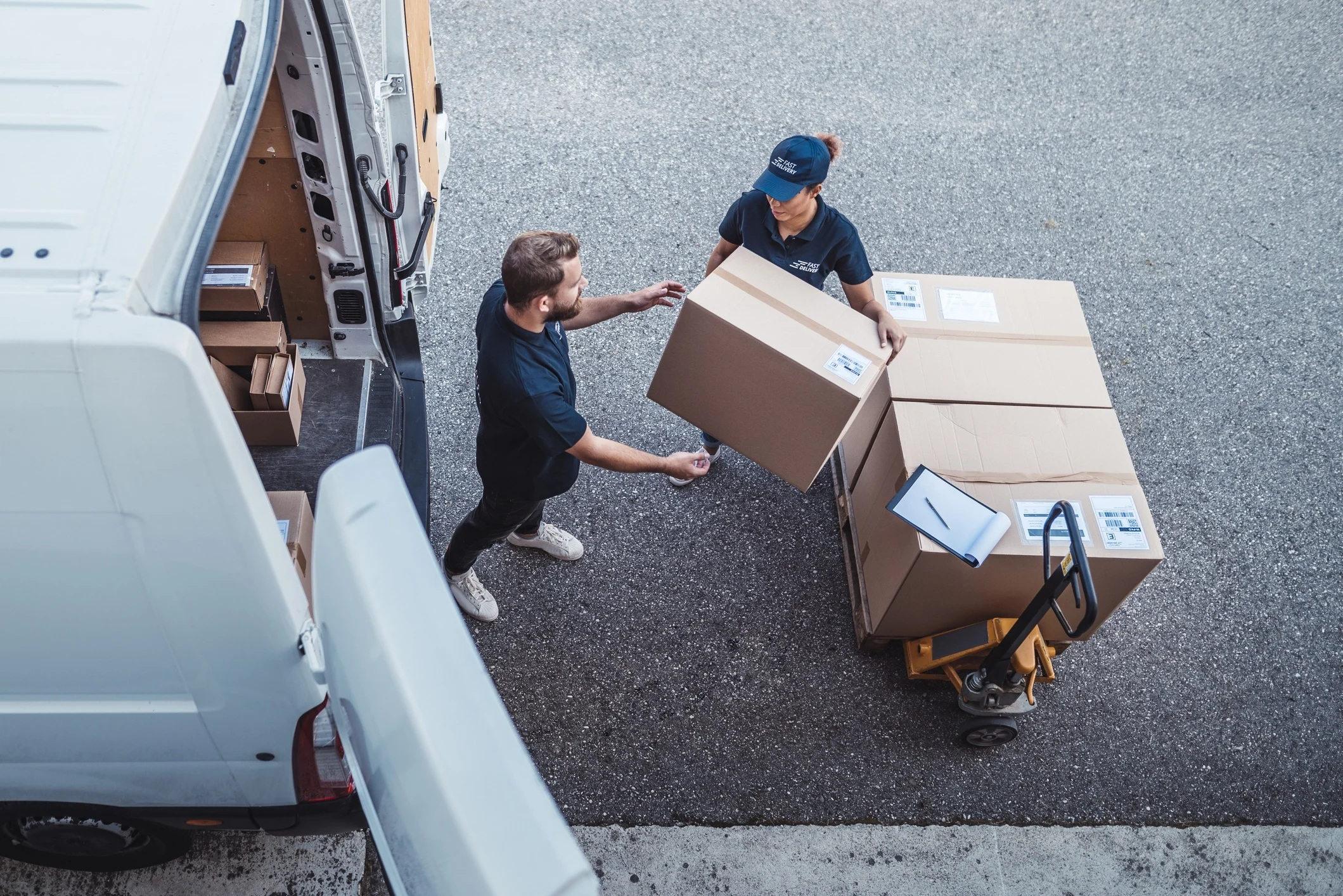 Looking down from above. Two people loading cartons frm a pallet into a white mini van.